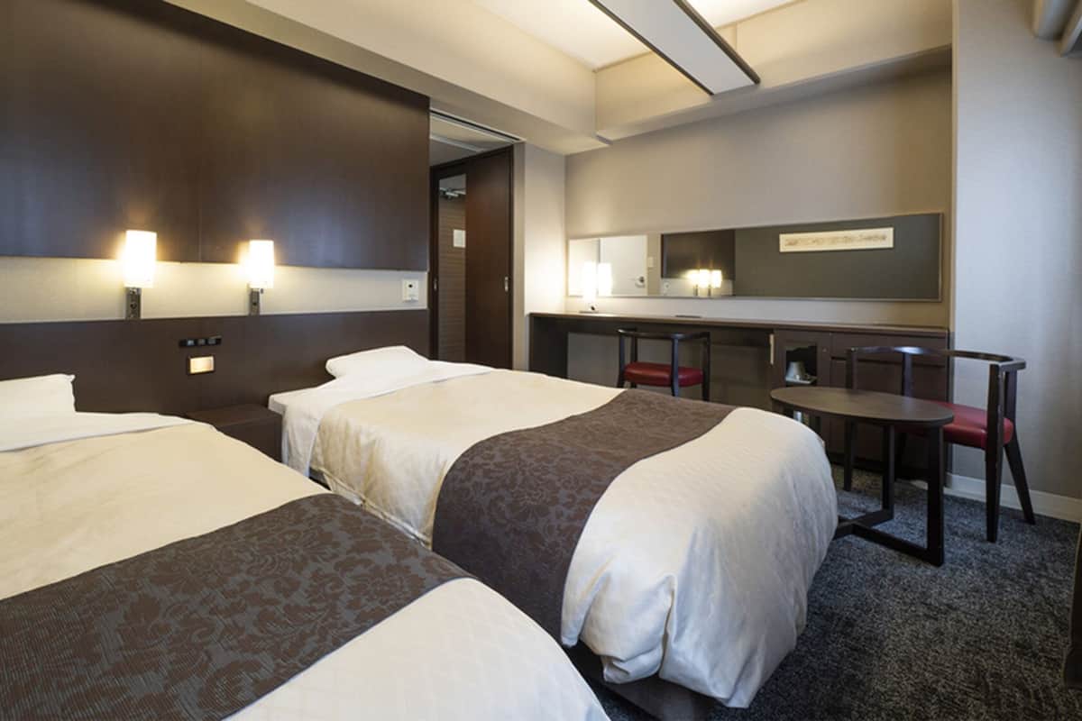 Une chambre d’hôtel avec deux lits, un bureau, une chaise et un miroir.