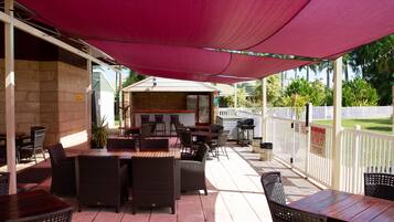 An outdoor patio with wicker furniture, a barbecue area, and a white picket fence.