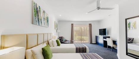 A hotel room with two beds, a desk, a television, and artwork on the walls.