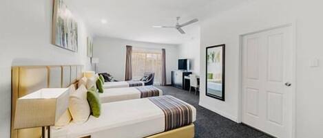 A hotel room with two beds, a desk, a chair, a TV, and a ceiling fan.
