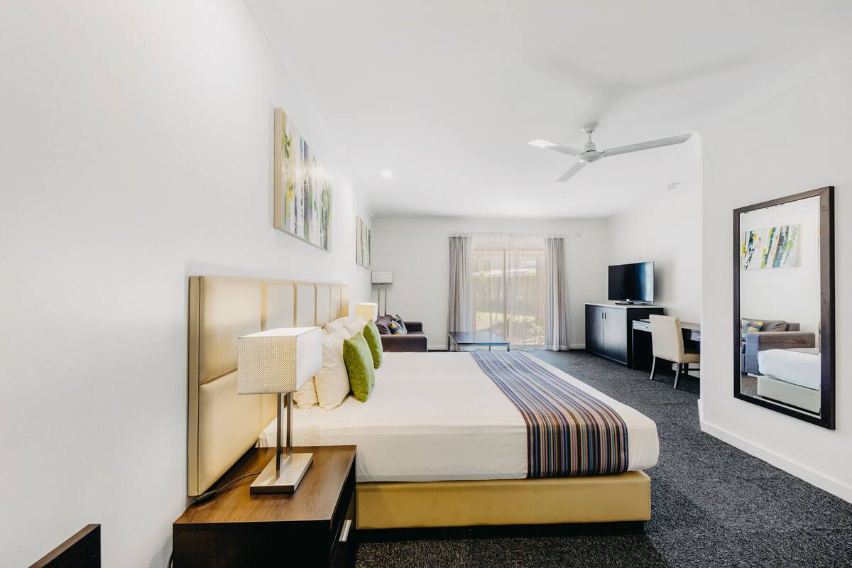 Habitación de hotel con cama, escritorio, silla, televisor y obras de arte en las paredes.