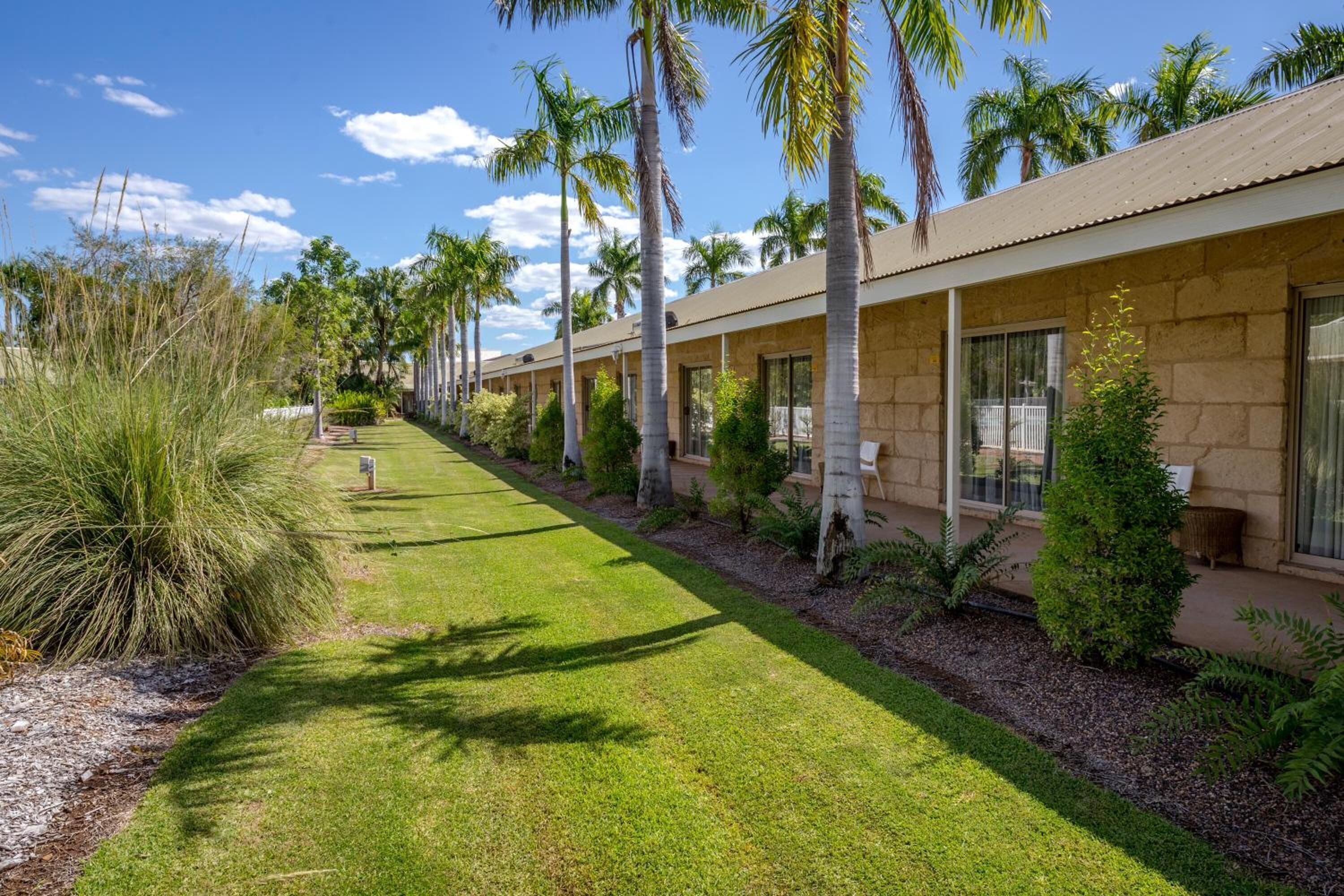 A row of single-story buildings with large windows, surrounded by well-maintained lawns and palm trees.