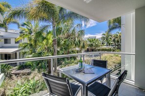 A balcony with a table and chairs, overlooking a lush garden with palm trees and other greenery. - Coolum at the Beach (Coolum Beach)