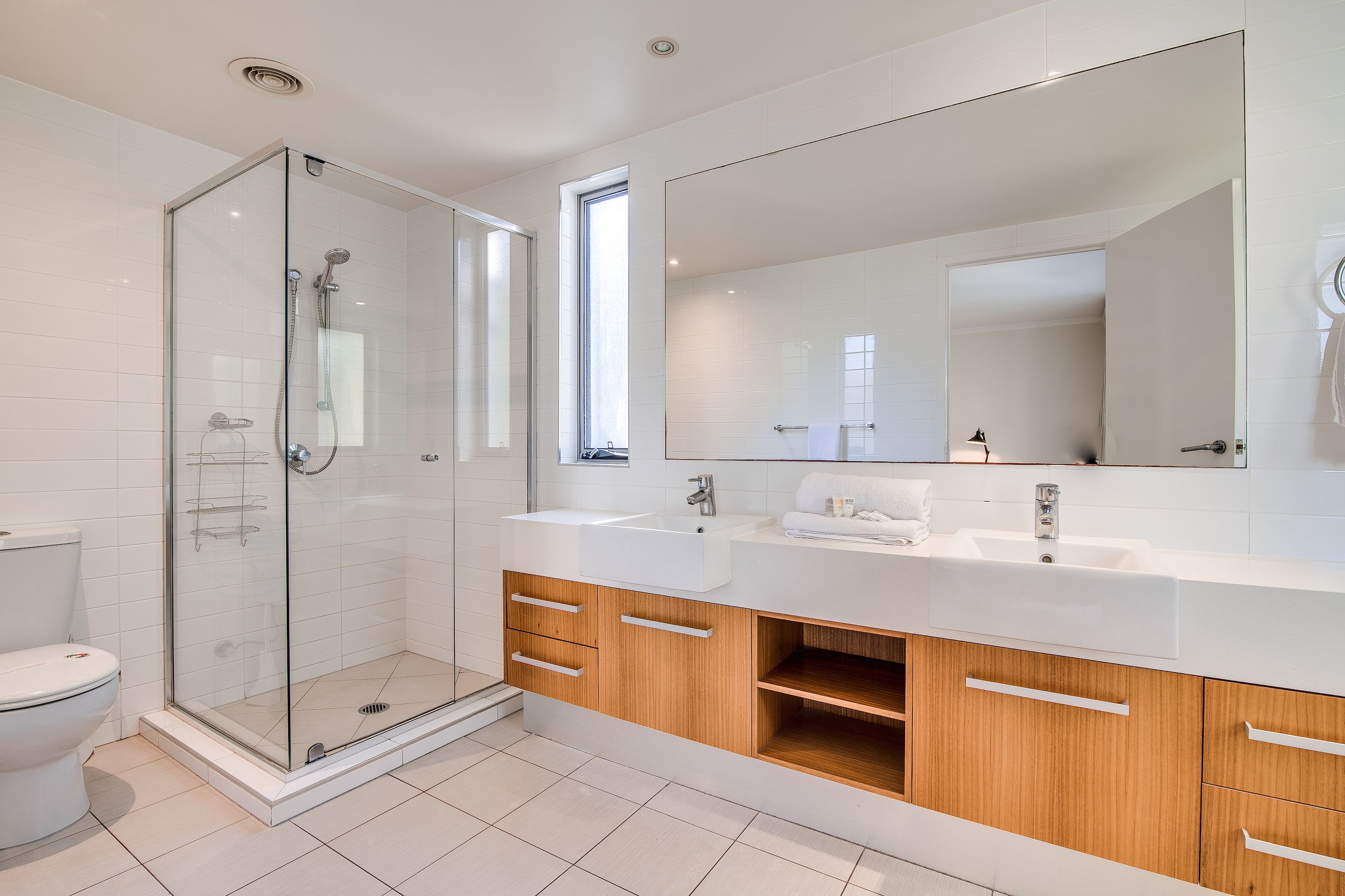 Ein modernes Badezimmer mit einer Glaskabine zur Dusche, einem großen Spiegel und Holzschränken.