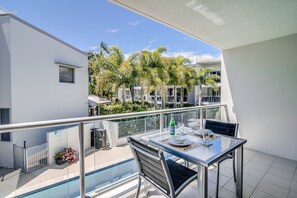 A balcony with a glass table, chairs, and a pool. - Coolum at the Beach (Coolum Beach)