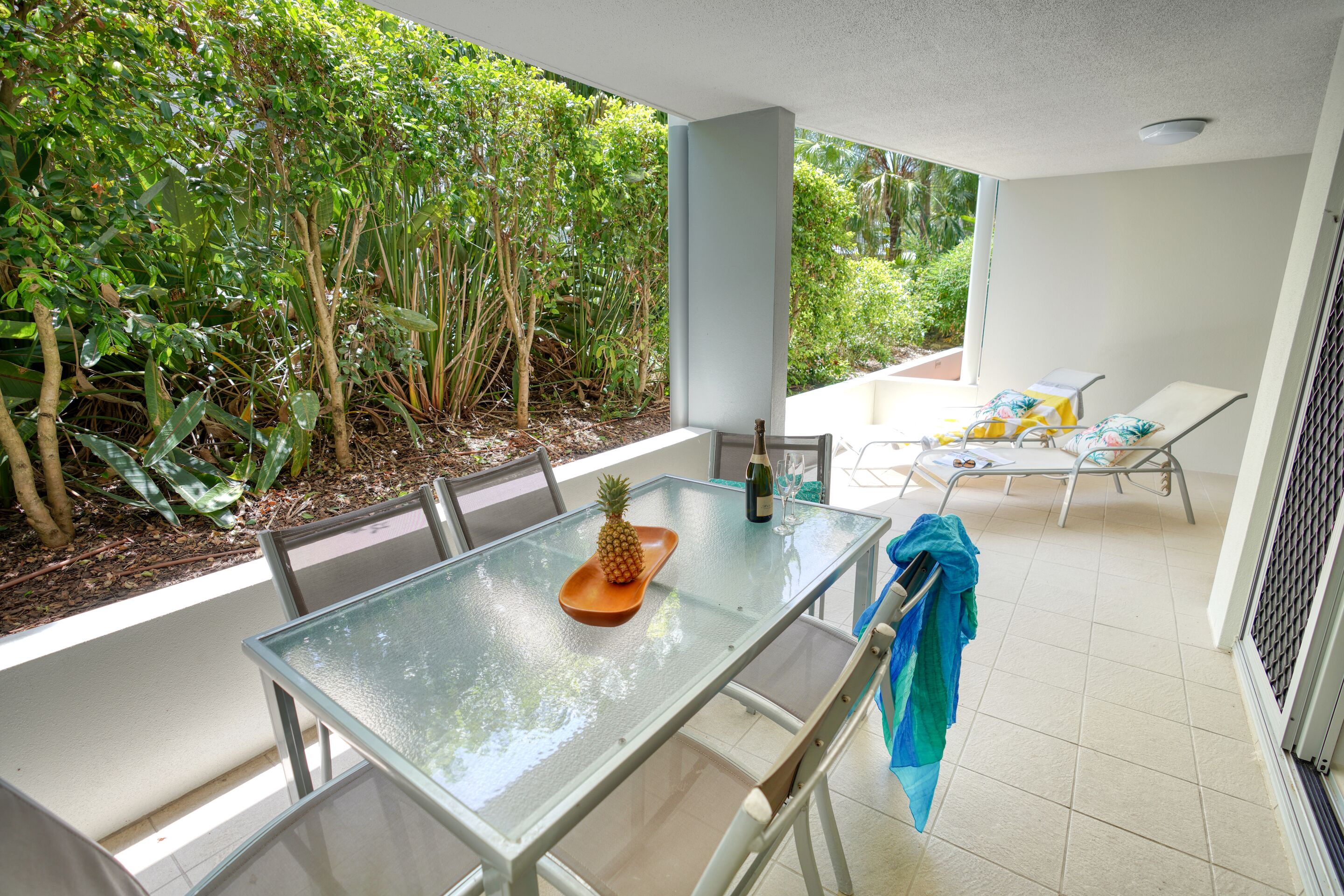 A glass-top table with chairs, a pineapple, and a bottle on it.
