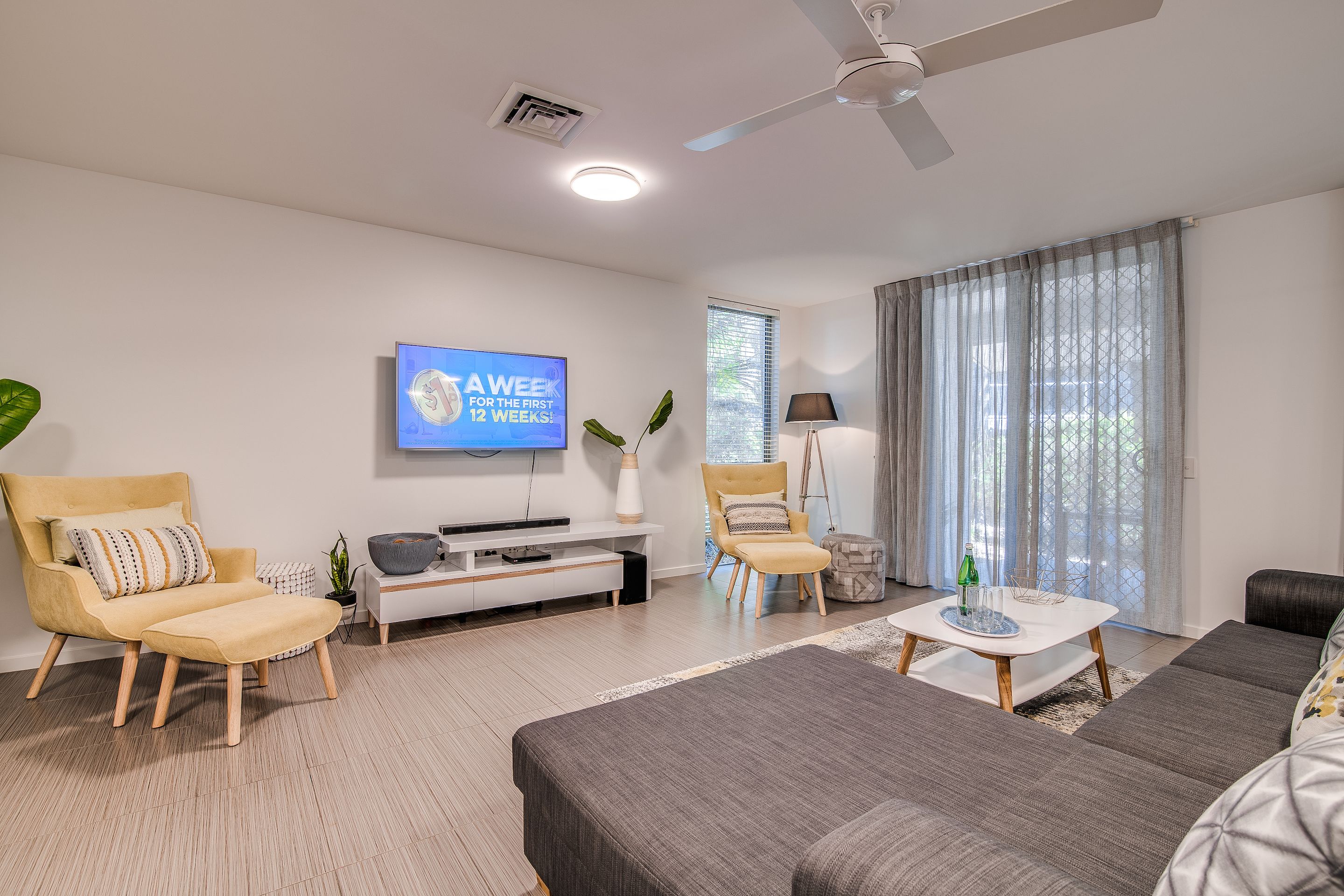 A modern living room with a sofa, chairs, a coffee table, a TV, and a window with curtains.