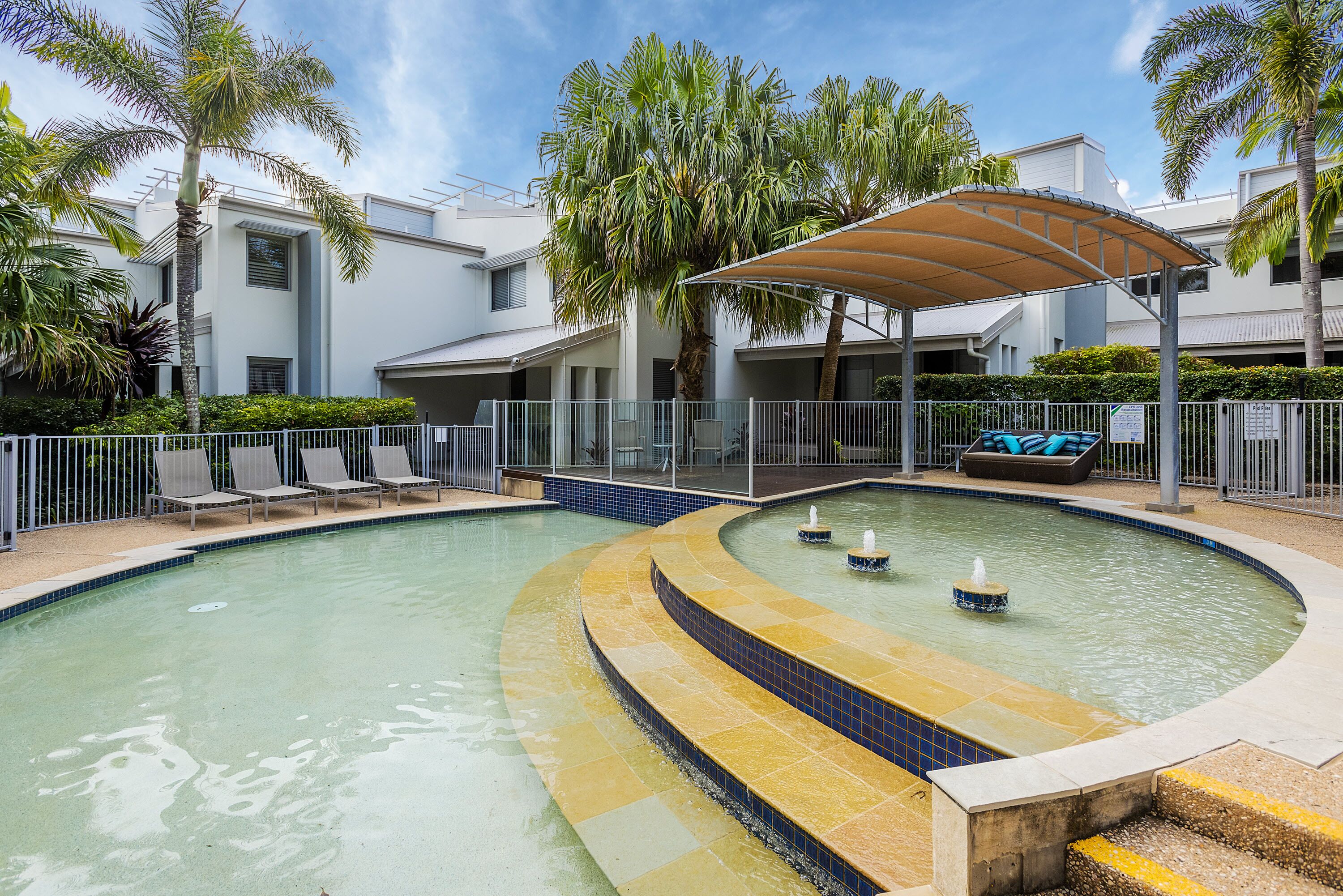 Ein Pool mit geschwungener Form, umgeben von Liegestühlen und einer überdachten Sitzgruppe.