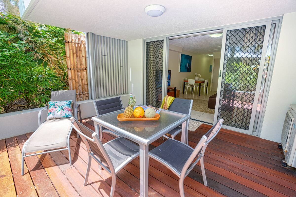 An outdoor patio with a table and chairs, a small grill, and a sliding glass door leading to an indoor area.