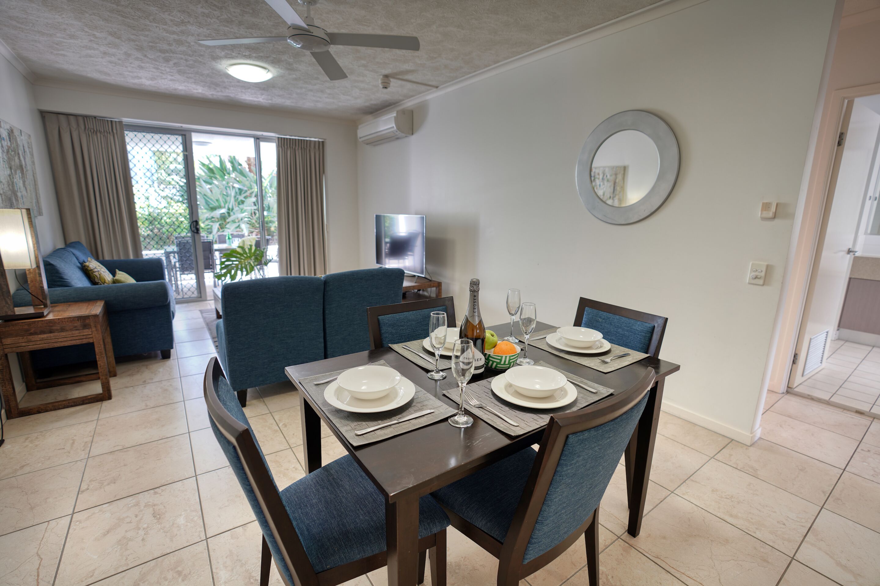 Un comedor con una mesa preparada para cuatro personas, un sofá y un televisor al fondo.