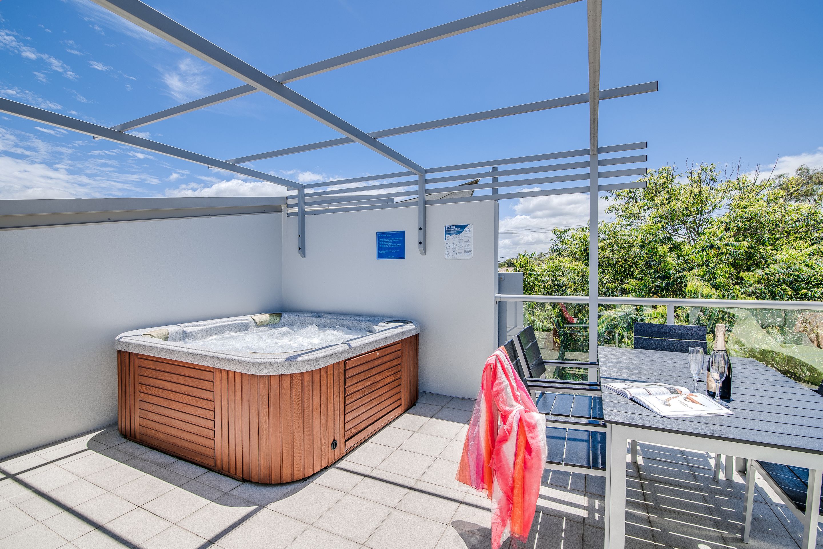 A rooftop terrace with a hot tub, a table with a bottle and glasses, and a chair.