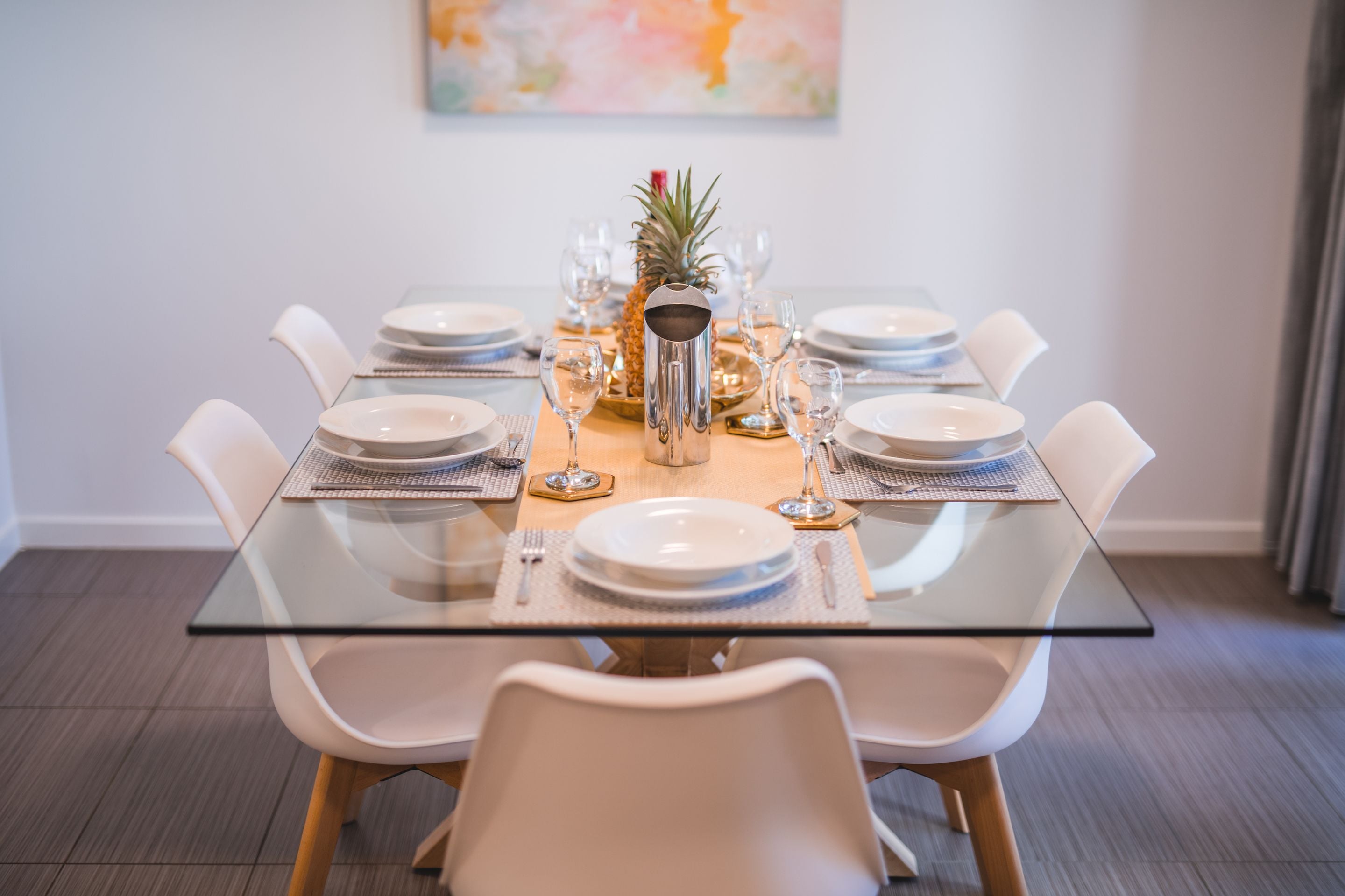 A dining table set with white plates, glasses, and a pineapple centerpiece.