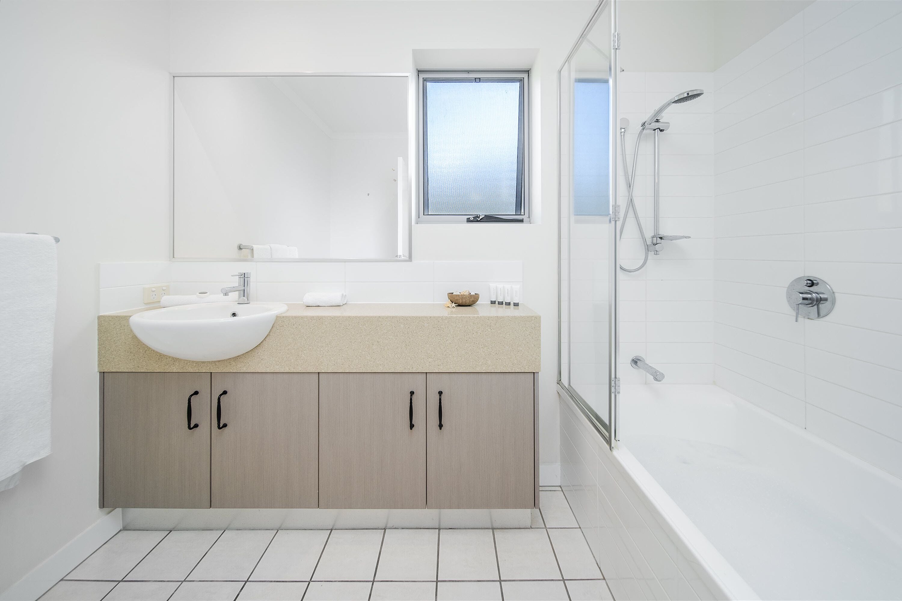 Un bany modern amb una banyera gran, un armari de dutxa de vidre i una finestra sobre el lavabo.