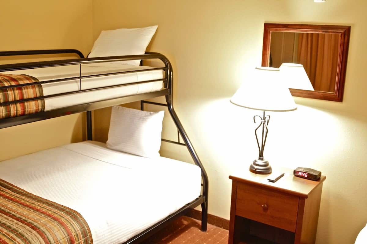 A bunk bed with a plaid blanket, a bedside lamp, a small wooden nightstand, and a mirror on the wall.