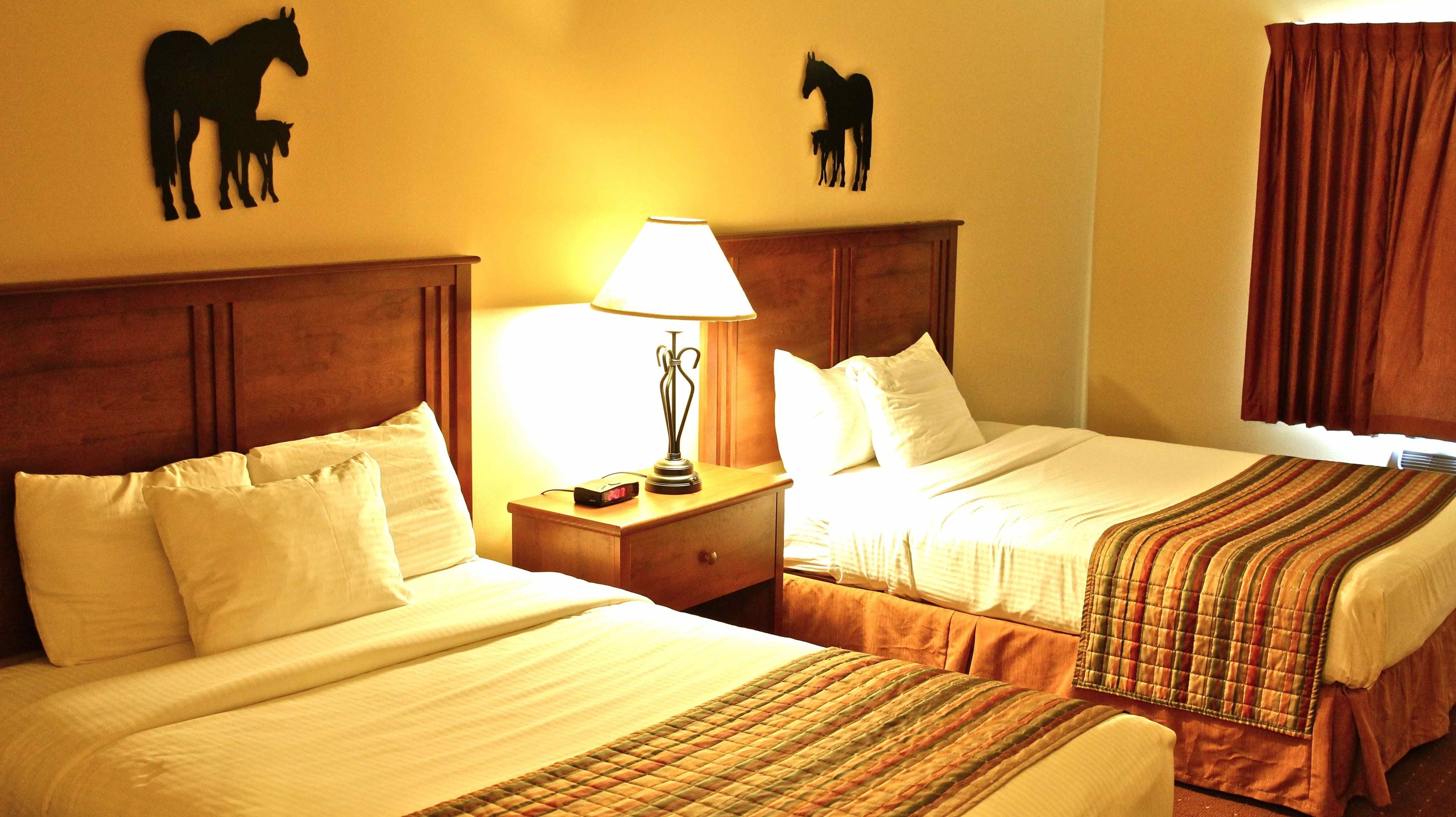 A hotel room with two beds, a nightstand with a lamp, and horse silhouettes on the walls.