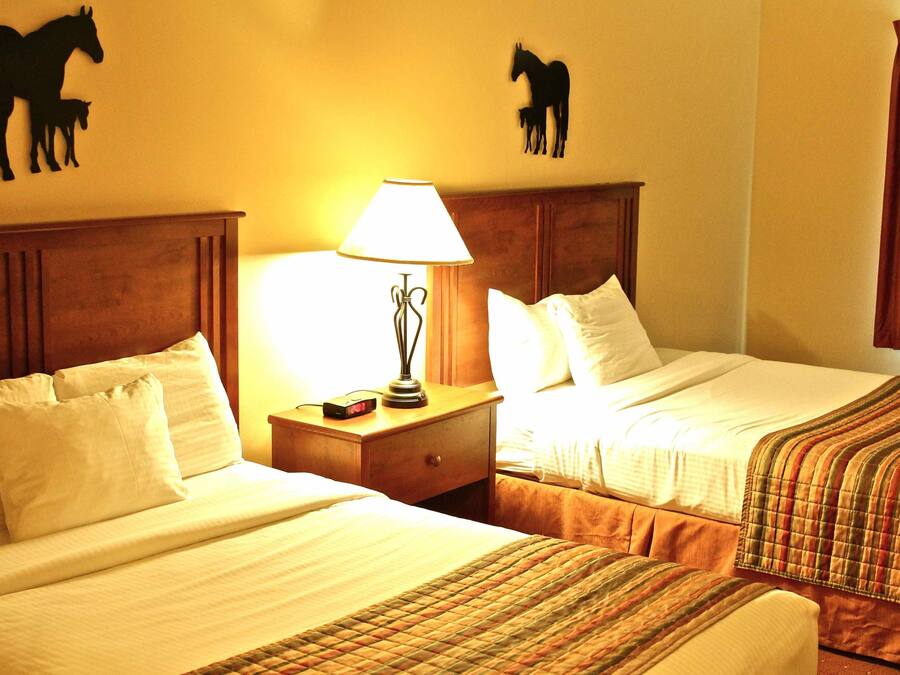 A hotel room with two beds, a nightstand with a lamp, and horse silhouettes on the walls.