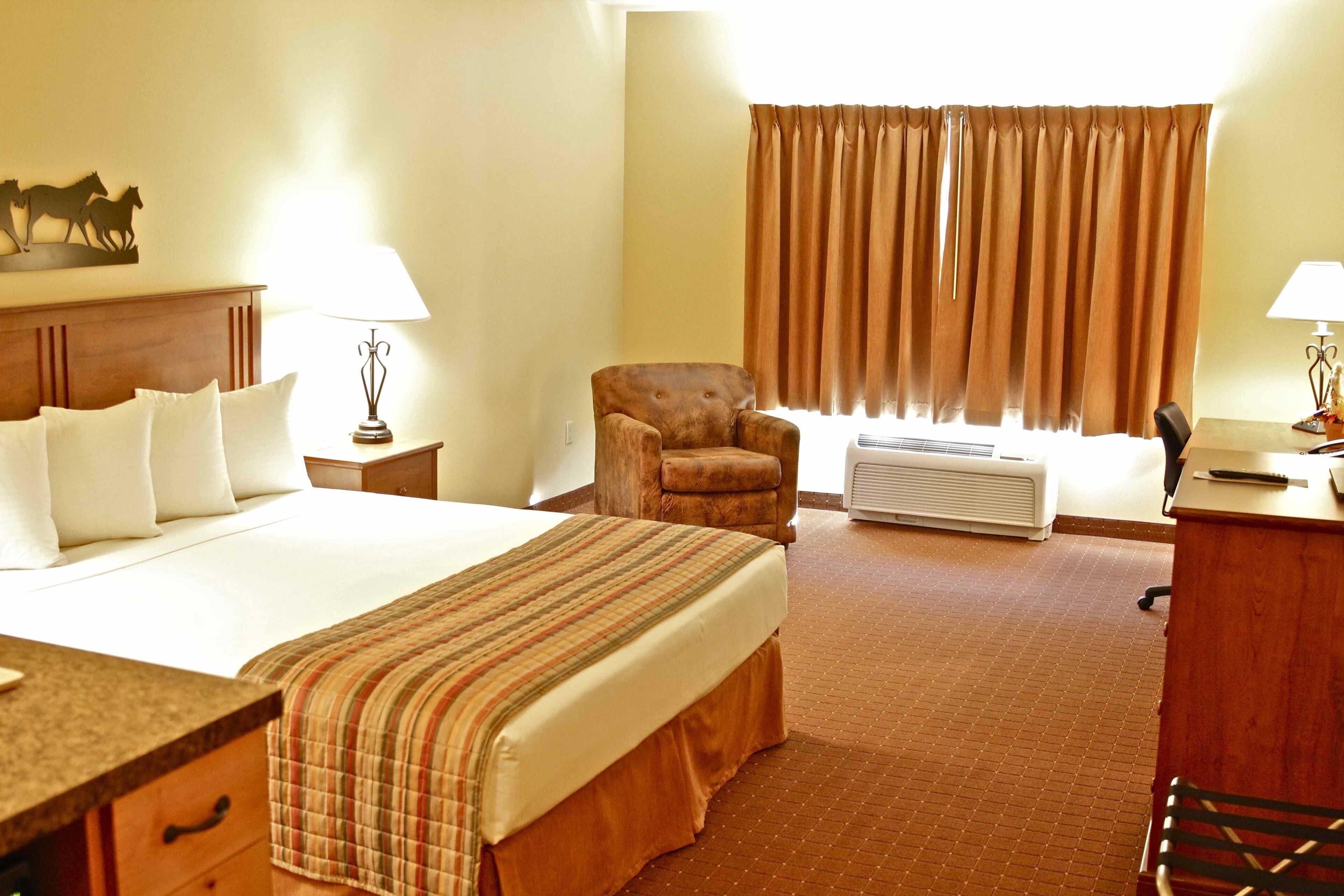 Una habitación de hotel con una cama grande, una silla, un escritorio y un ventanal con cortinas.