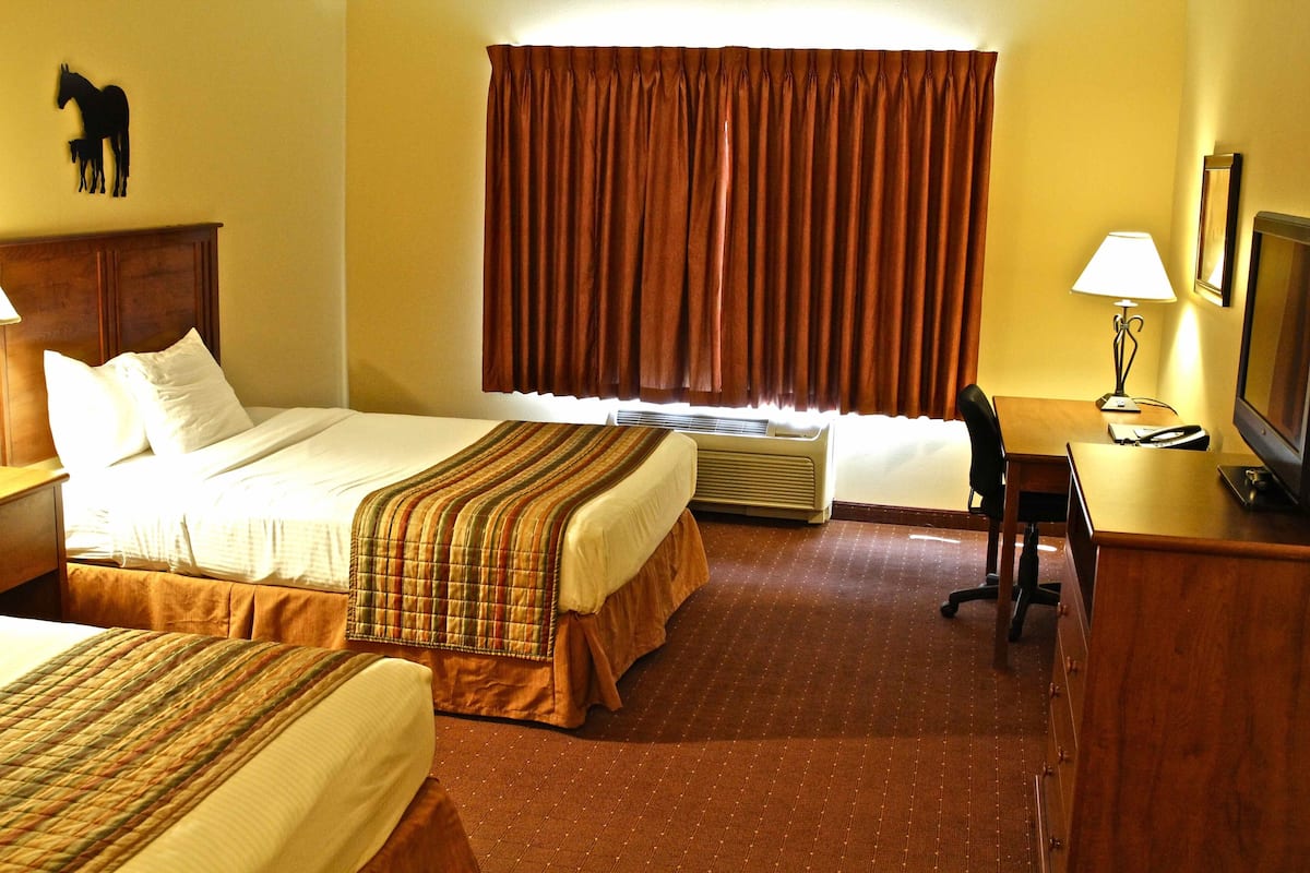 A hotel room with two beds, a desk, a chair, a television, and a window with curtains.