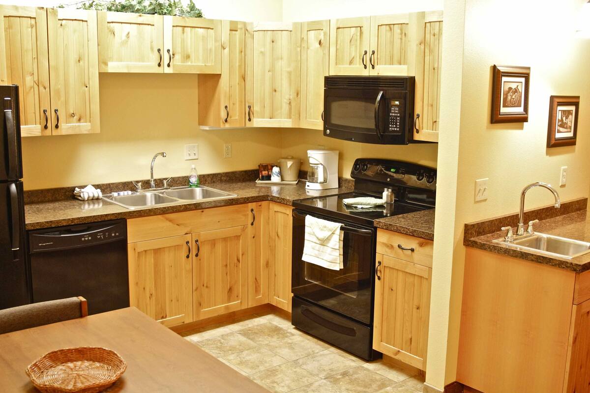 A kitchen with wooden cabinets, a black microwave, a stove, and a dishwasher.