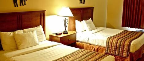 Two double beds with white linens, a wooden headboard, a bedside table with a lamp, and two wall-mounted horse silhouettes.