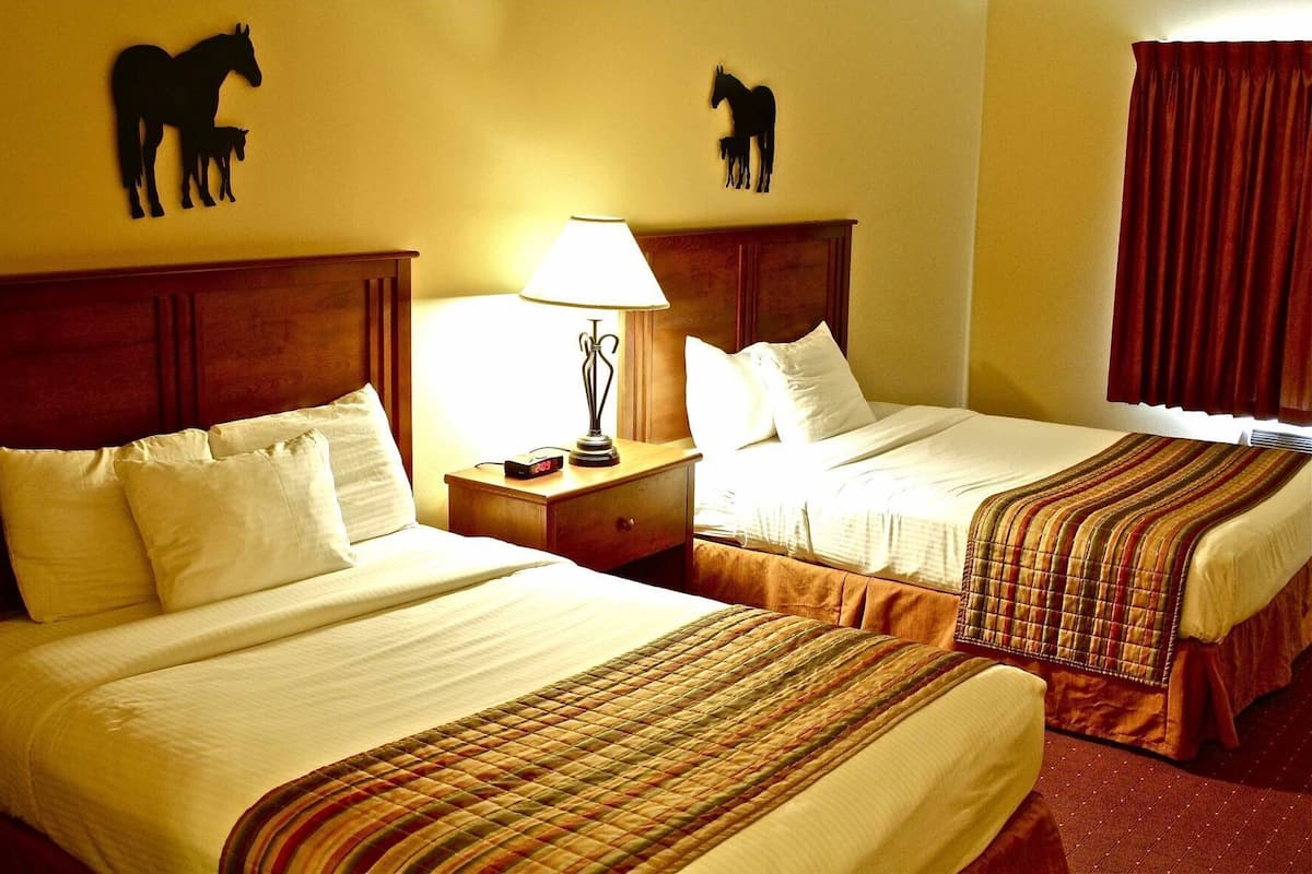 Ein Hotelzimmer mit zwei Betten, einem Nachttisch mit Lampe und Wandbildern von Pferden.
