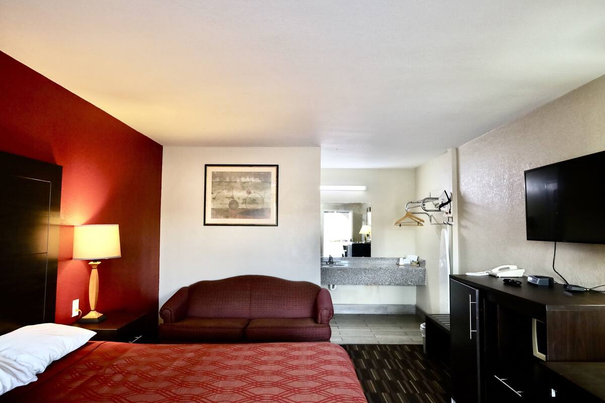 Une chambre d’hôtel avec un lit, un canapé, un bureau avec une télévision, une lampe et un tableau au mur.