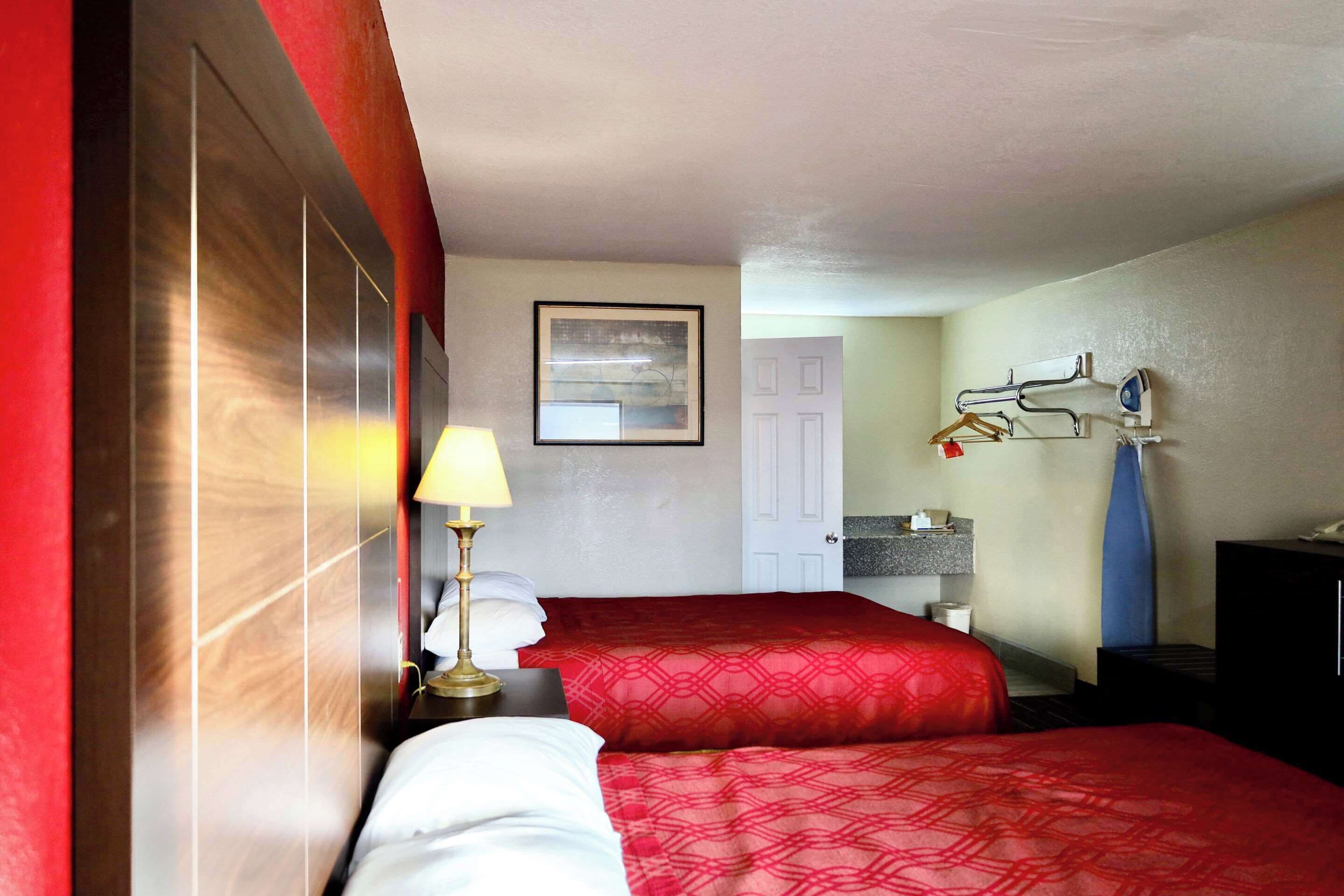 Hotelkamer met twee bedden, een nachtkastje met een lamp, een lijst op de muur, een badkamer met een handdoekrek en een kast.