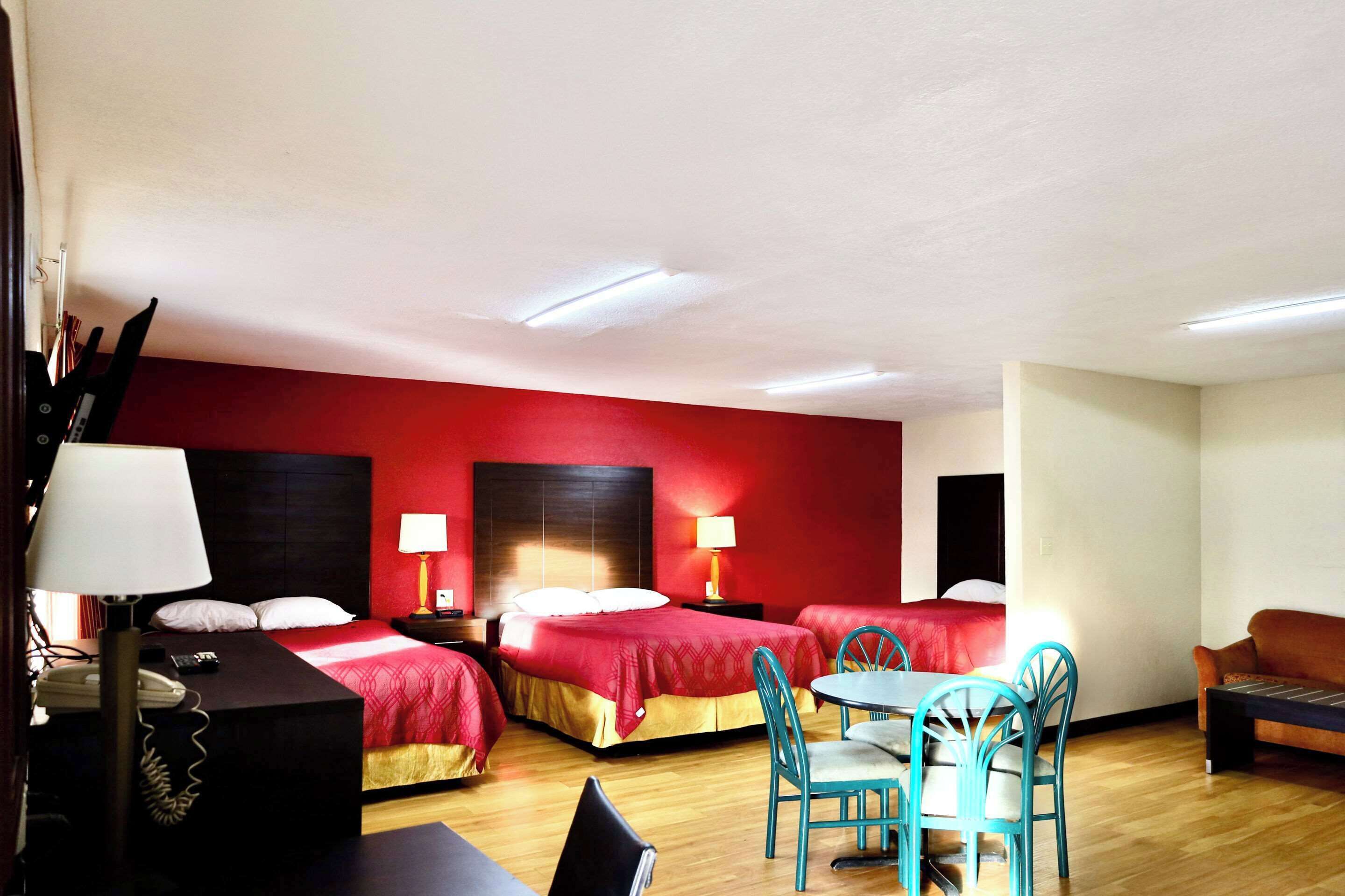 A hotel room with three beds, a dining table with chairs, a sofa, and a telephone.