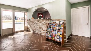 A lobby with a herringbone floor, a stone wall, a fireplace, and a magazine rack. - Rodeway Inn Pauls Valley (Pauls Valley)
