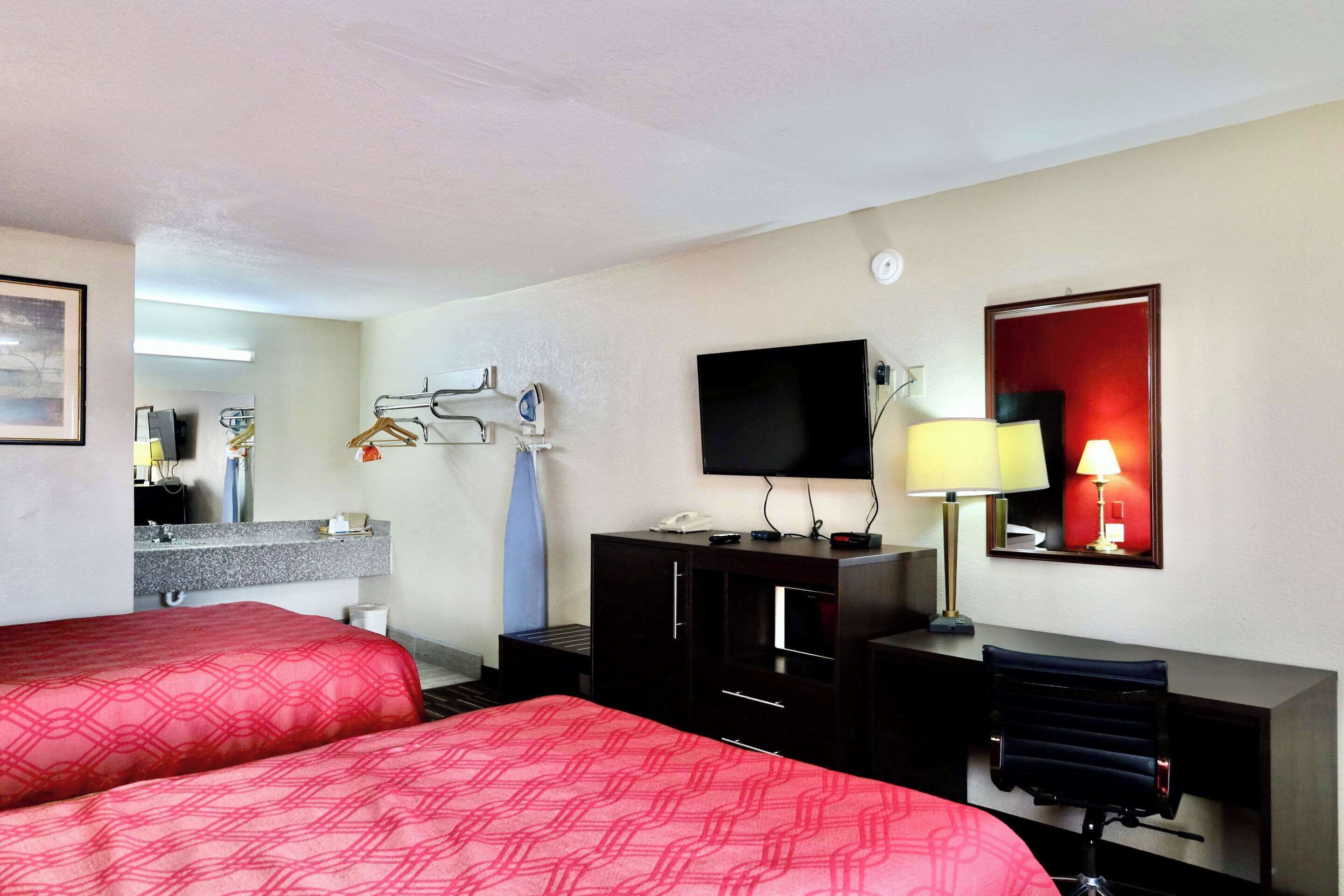 Quarto de hotel com duas camas, uma escrivaninha, televisão, abajur e espelho.