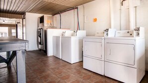 A laundry room with four white washers and dryers, a table, and a refrigerator. - Rodeway Inn Pauls Valley (Pauls Valley)