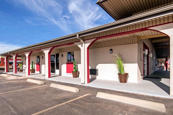 A row of hotel rooms with a covered outdoor area, each with a potted plant and a window.