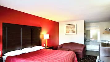 A hotel room with a large bed, a desk, a chair, a nightstand with a lamp, and a bathroom visible through an open door.