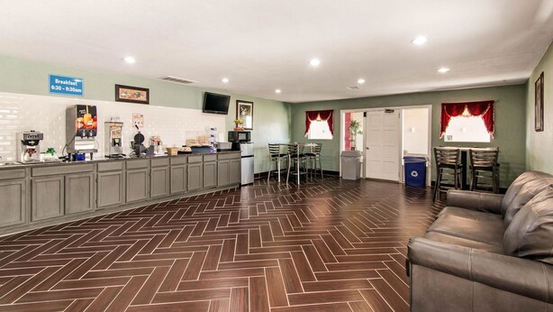 A reception area with a herringbone patterned floor, a counter with a breakfast sign, and a leather couch. - Rodeway Inn Pauls Valley (Pauls Valley)