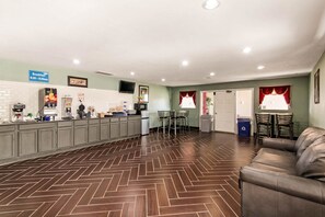 A reception area with a herringbone patterned floor, a counter with a breakfast sign, and a leather couch.