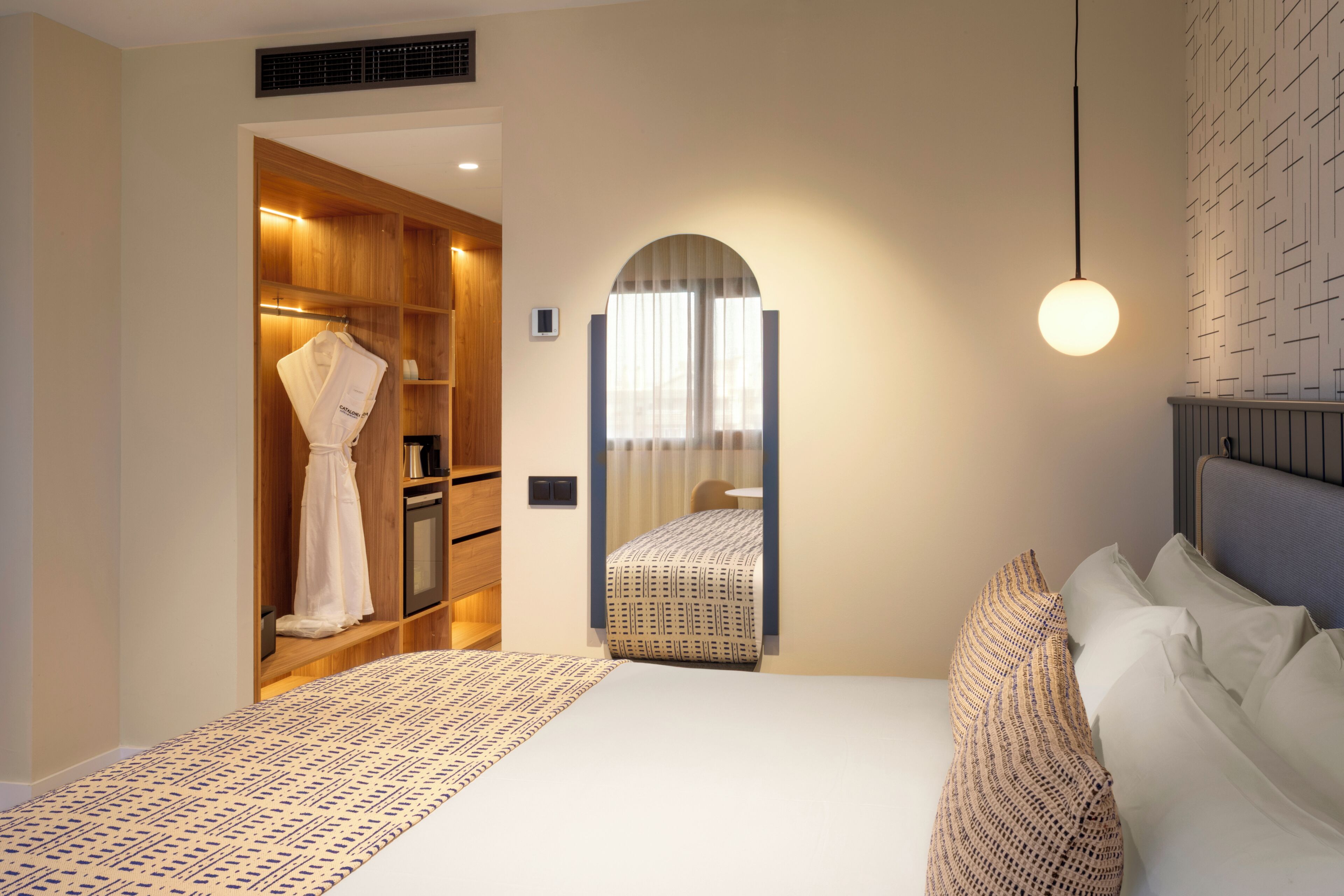 A bedroom with a bed, a wardrobe, a mirror, and a hanging light fixture.