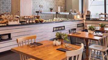 Un restaurante con mesas y sillas de madera, una barra de buffet con diferentes platillos, y un muro con diseño.