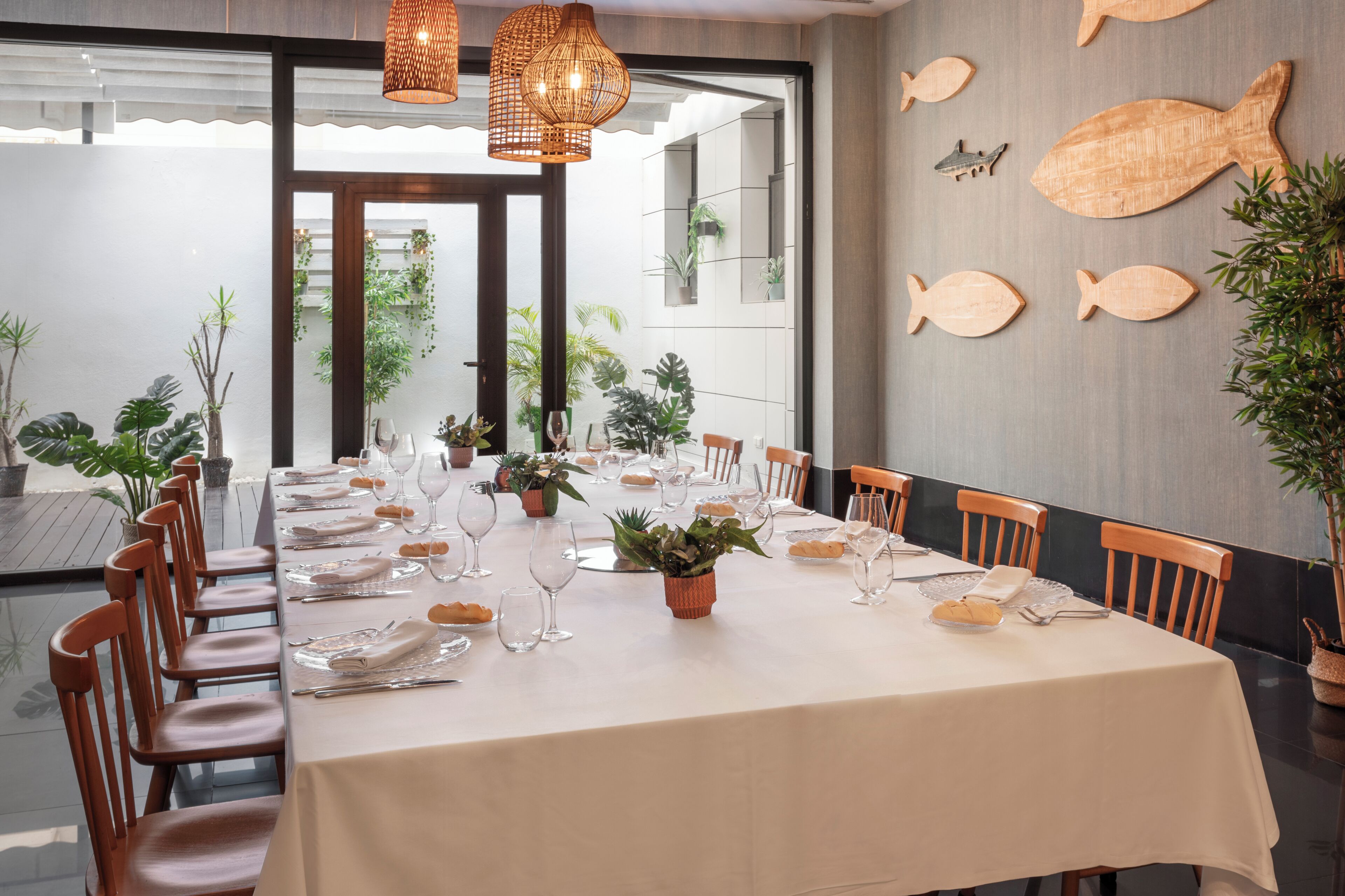 Un coin repas avec une longue table dressée pour le repas, des chaises en bois et un mur décoré de motifs représentant des poissons.
