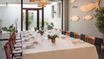 Un coin repas avec une longue table dressée pour le repas, des chaises en bois et un mur décoré de motifs représentant des poissons.