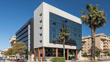 A modern building with a glass facade, multiple floors, and a parking area with cars.