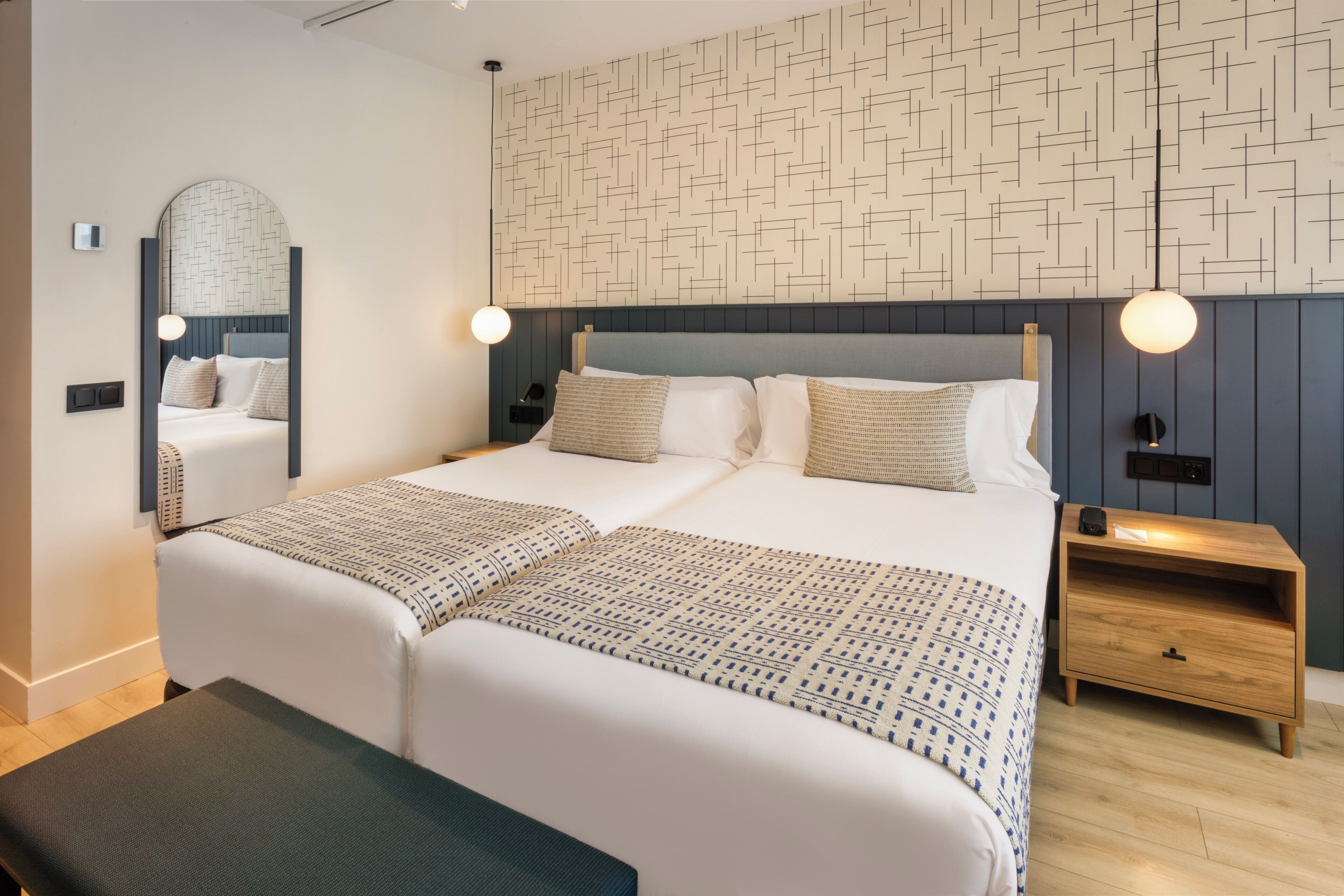 Una habitación de hotel moderna con una cama grande, mesitas de noche, un espejo y una pared con diseño.