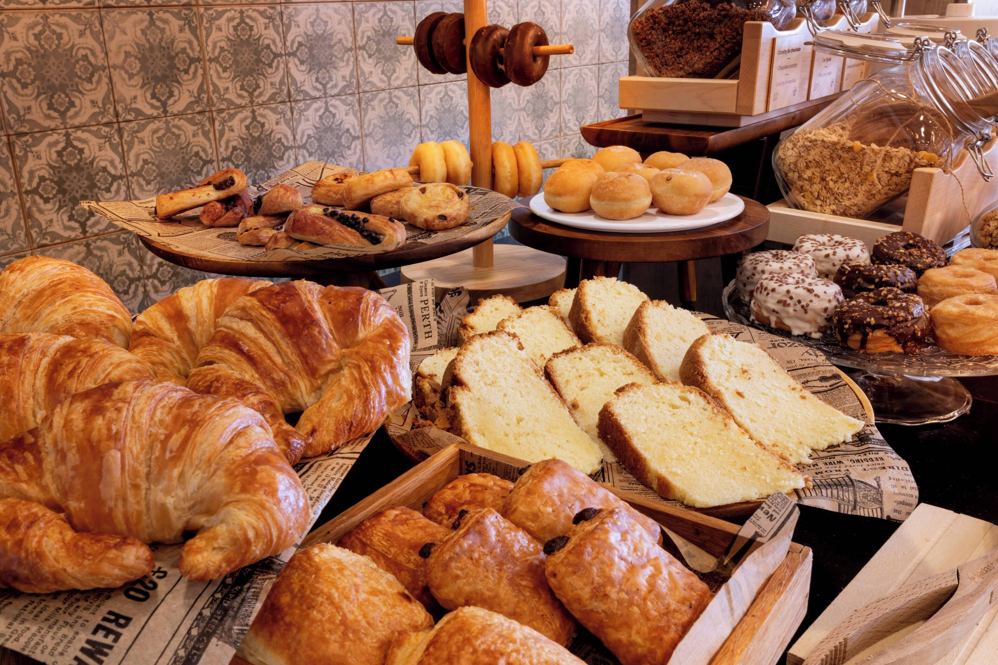 Eine Auswahl an Backwaren, darunter Croissants, Brot und Gebäck, präsentiert auf einer Theke mit Fliesenwand.
