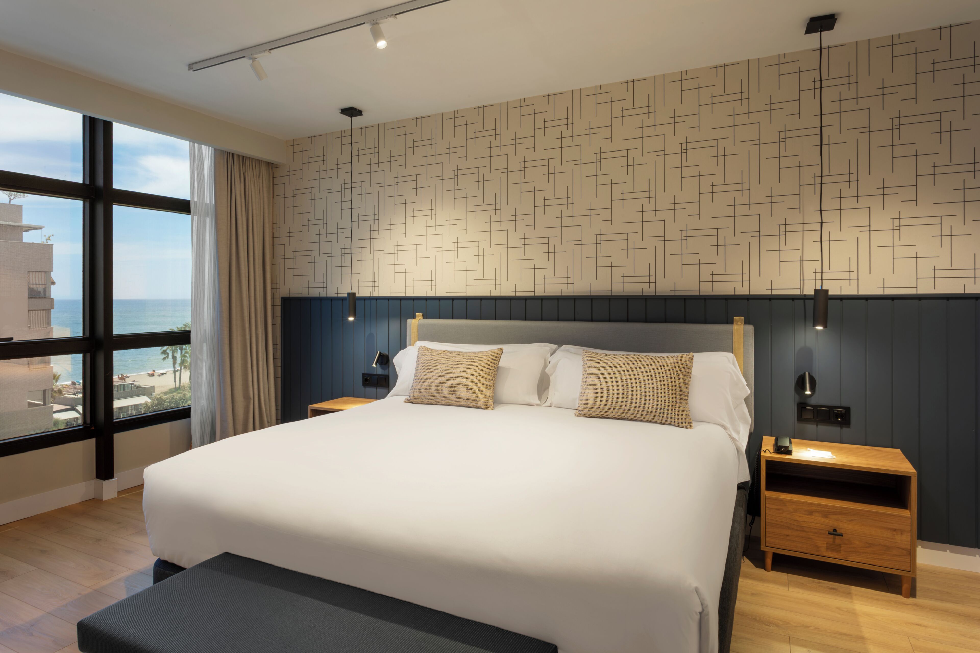 Et moderne hotelværelse med en stor seng, havudsigt og en væg med et geometrisk mønster.