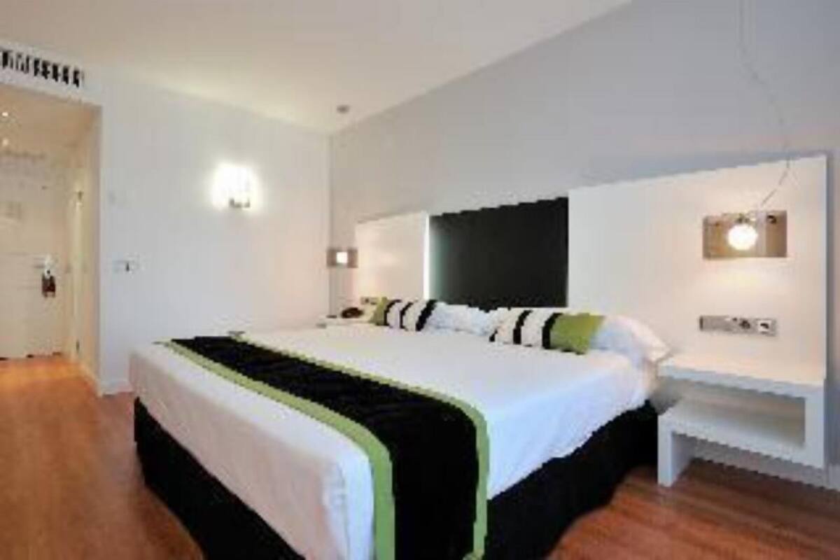 A modern hotel room with a large bed, bedside tables, and wall-mounted lighting.