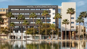 Un hotel modern amb una piscina al davant, envoltat de palmeres i altres edificis.