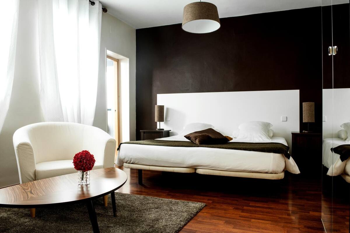 A modern bedroom with a large bed, bedside lamps, a white sofa, and a round coffee table.
