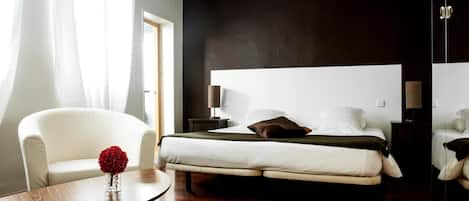A modern bedroom with a large bed, bedside lamps, a white sofa, and a round coffee table.