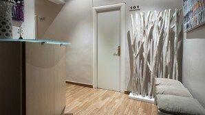 A hallway with a wooden floor, a reception desk, a white door, and a wall-mounted number sign. - THC Gran Via Hostel (Madrid)