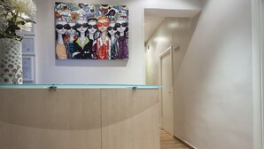 A hallway with a reception desk, a colorful artwork above it, and a door labeled "102". - THC Gran Via Hostel (Madrid)
