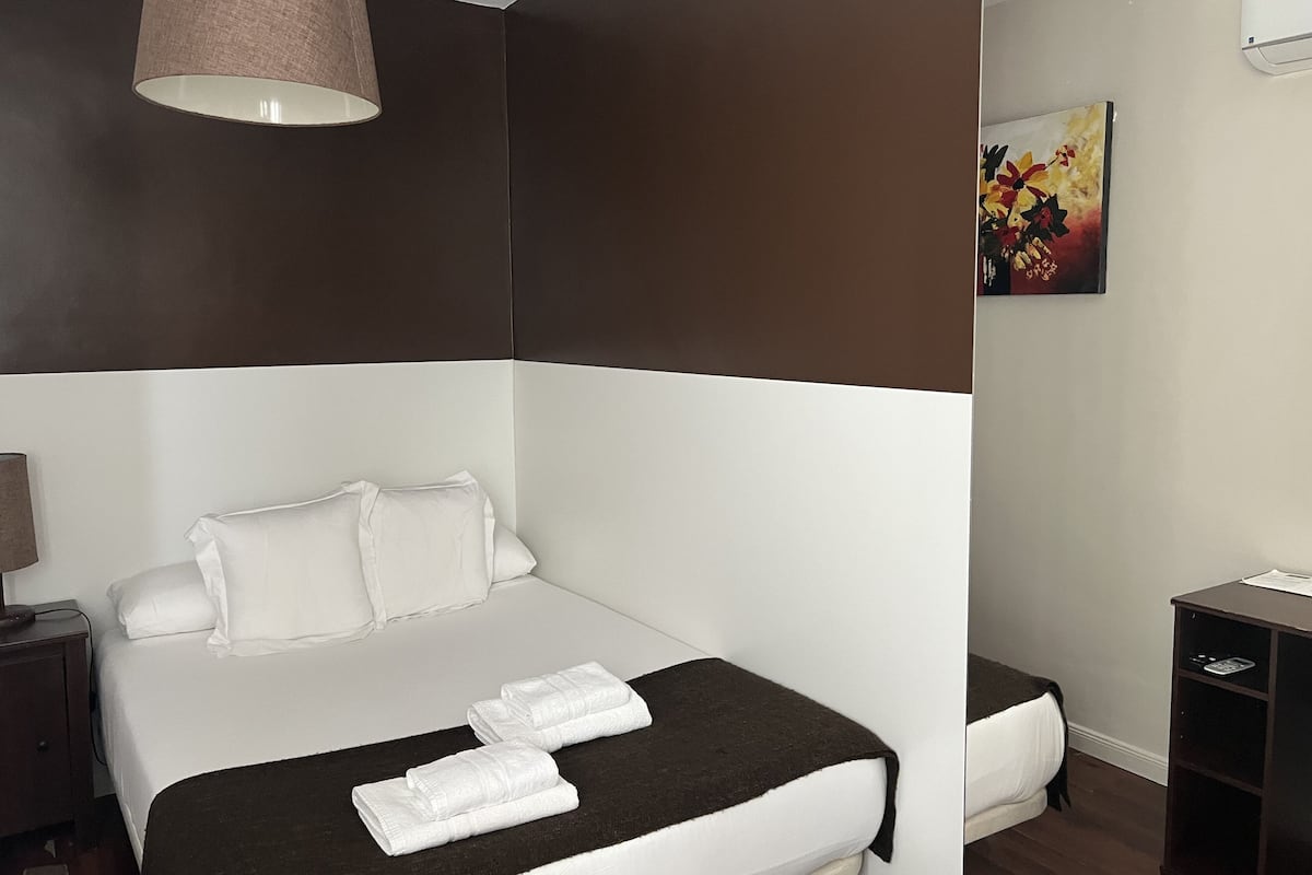 A modern hotel room with a large bed, a bedside table, a lamp, and a painting on the wall.